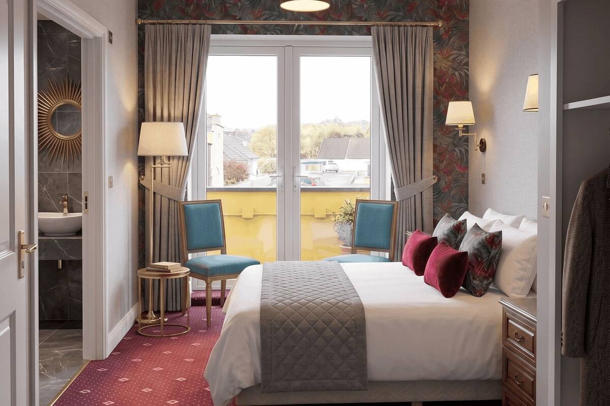 A hotel room with a bed, a sitting area with a chair and table, a window with curtains, and a view of the outside.