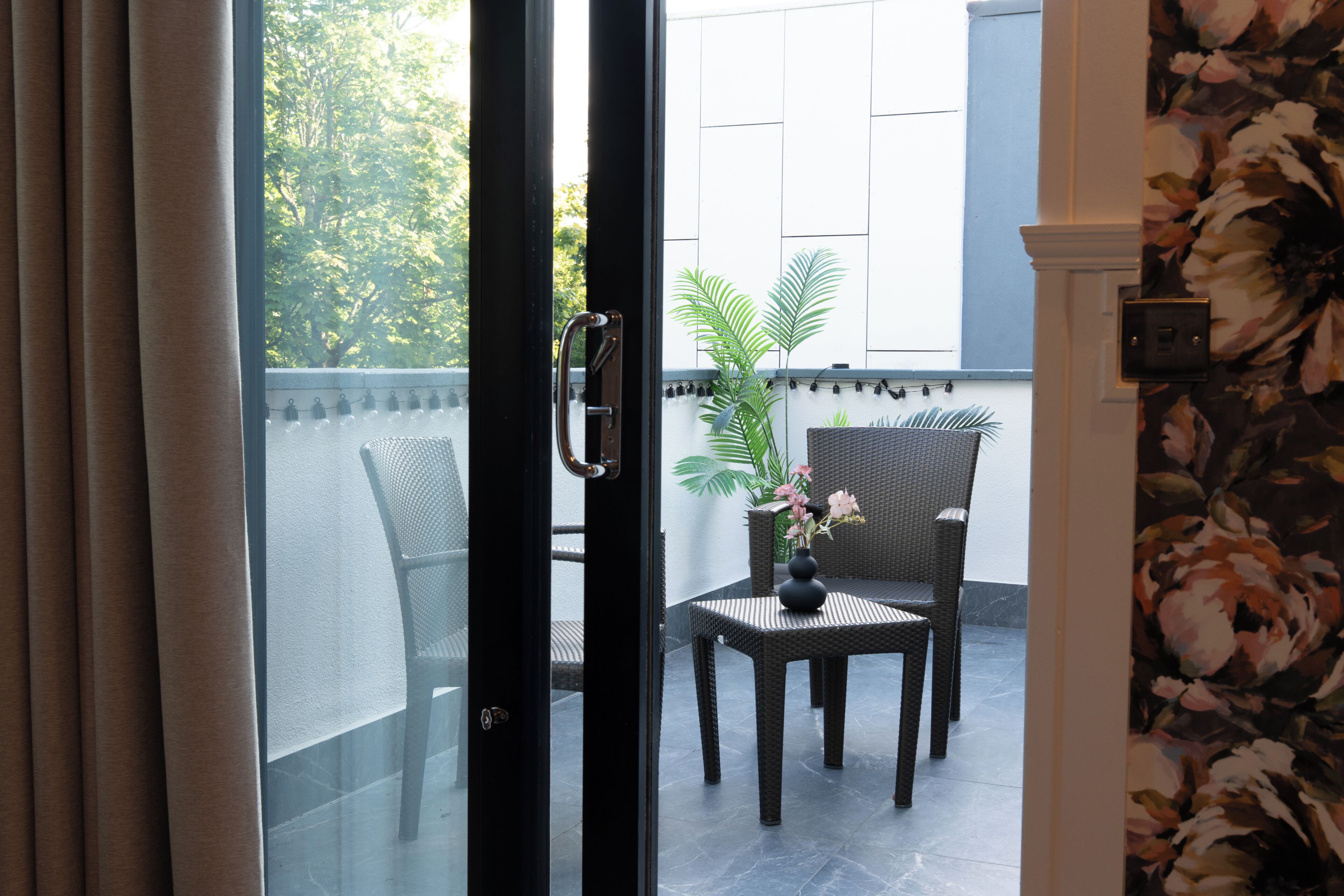 Habitación con puerta corrediza de vidrio que da a un espacio exterior con sillas de mimbre y una pequeña mesa.