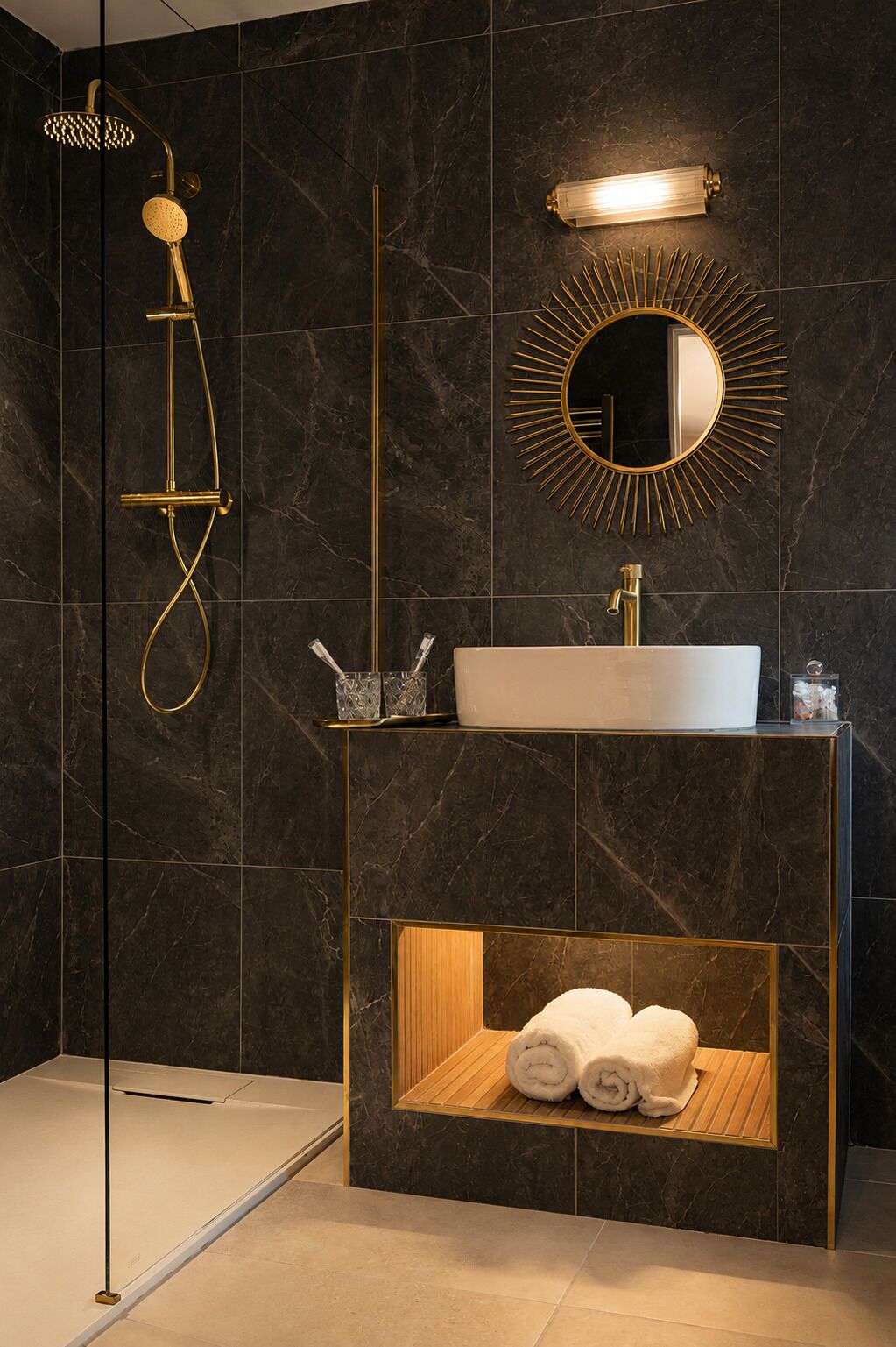 Un baño moderno con ducha dorada, lavamanos blanco y espejo con marco de sol.