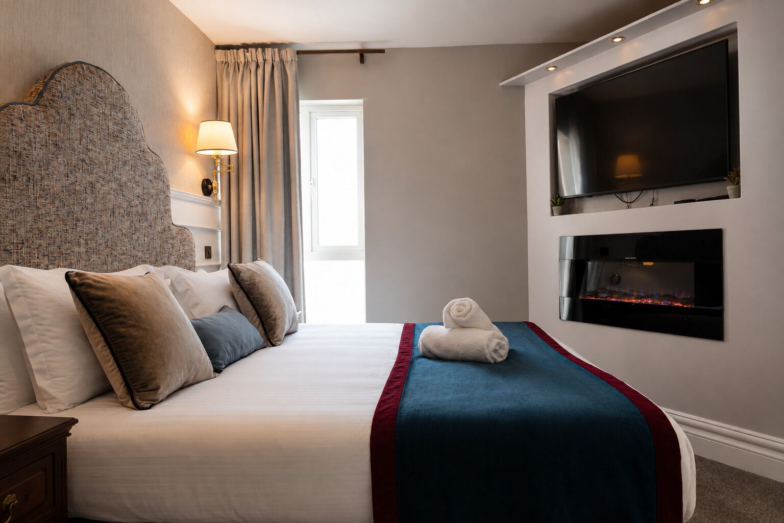 A hotel room with a large bed, a flat-screen TV, a fireplace, and a view of the outdoors.
