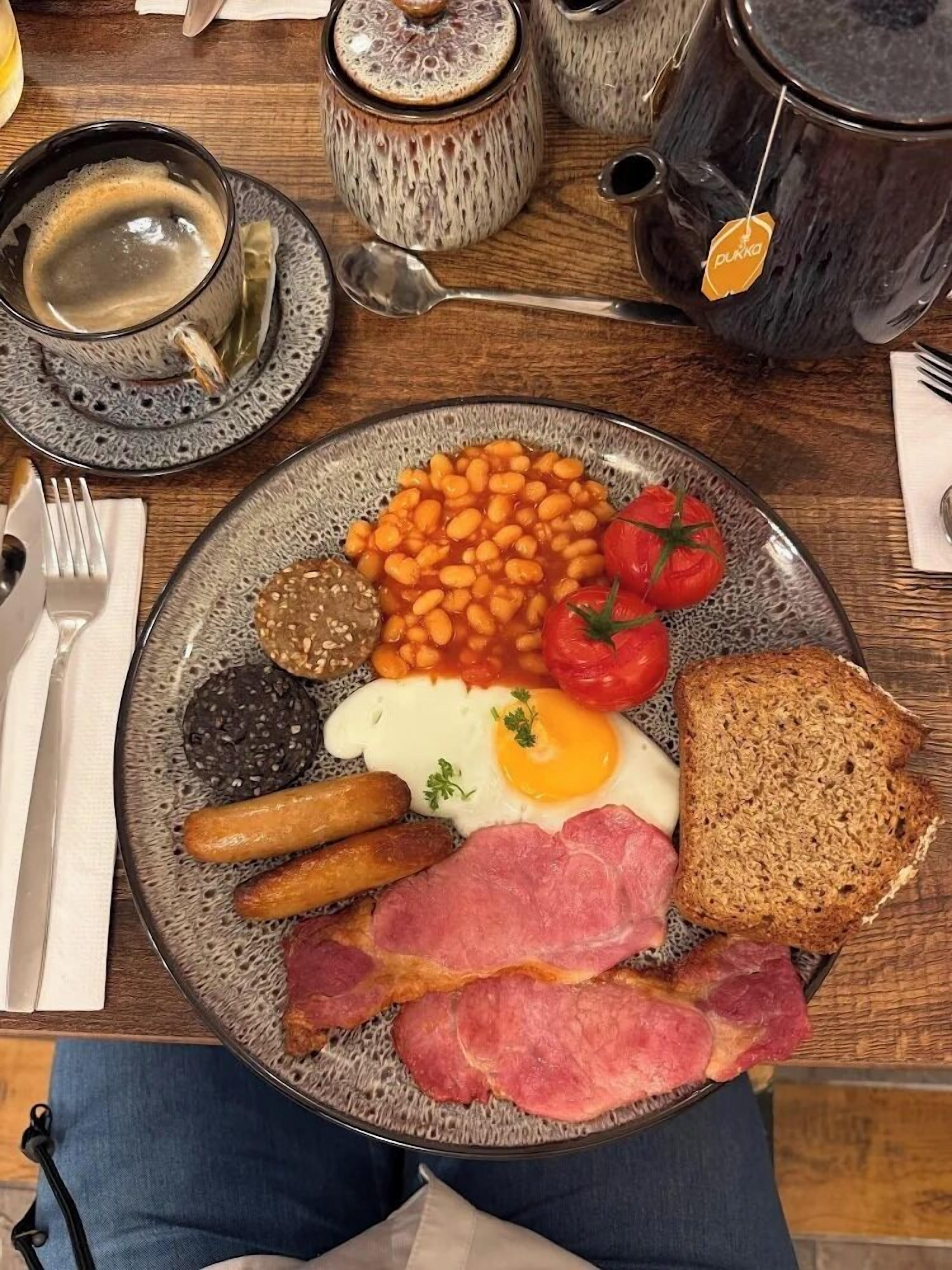 A plate of breakfast food including eggs, sausages, bacon, beans, tomatoes, and toast.