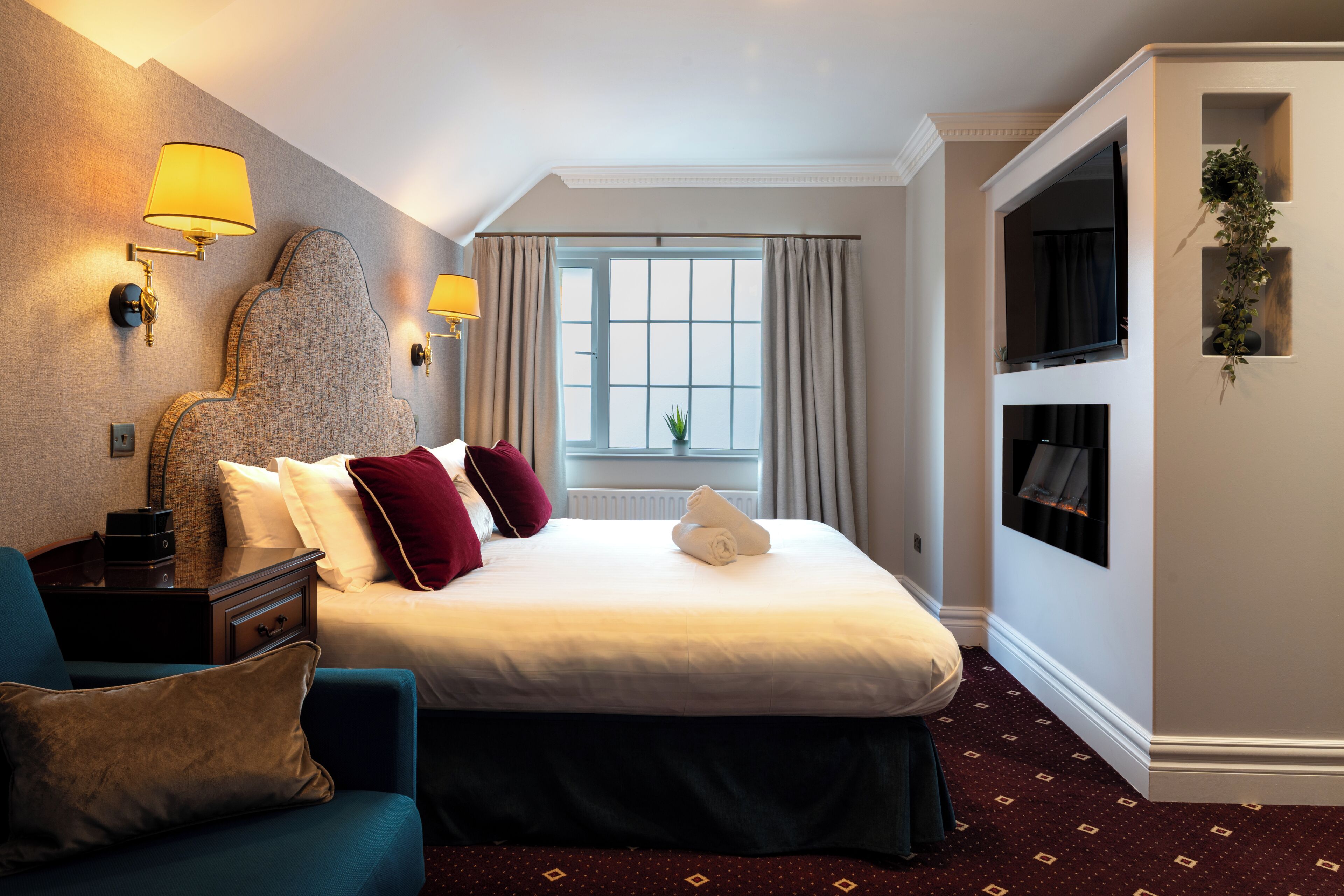 A hotel room with a bed, a desk, a chair, a TV, and a window with curtains.