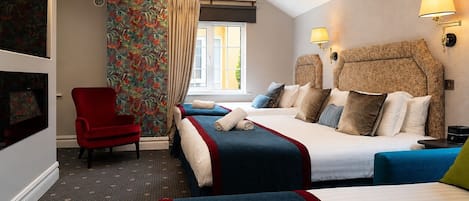 A hotel room with two beds, a red armchair, a large window with curtains, and wall-mounted lamps.