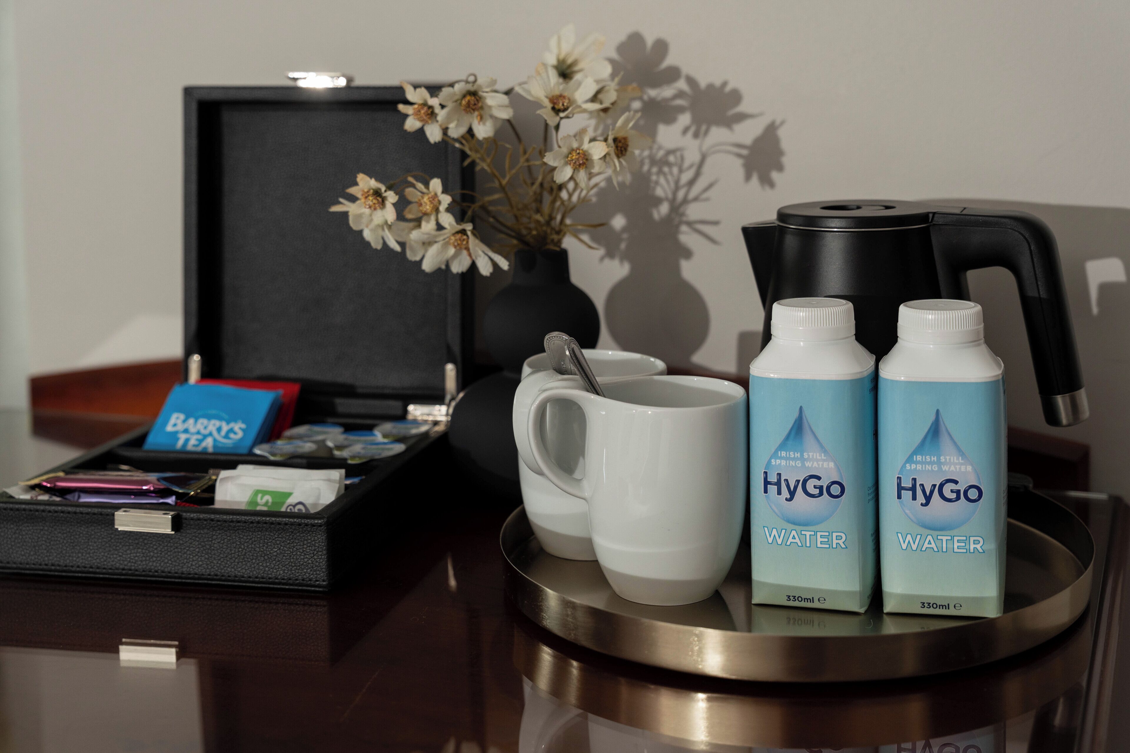 A tray with a mug, two bottles of HyGo water, a tea bag, and a small vase with flowers.