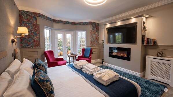 A hotel room with a bed, two chairs, a fireplace, a TV, and a view of the outside. - THE VÉRO (Killarney)