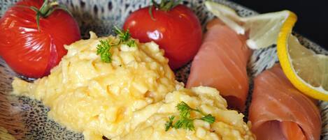Un plato con huevos revueltos, salmón ahumado y tomates.