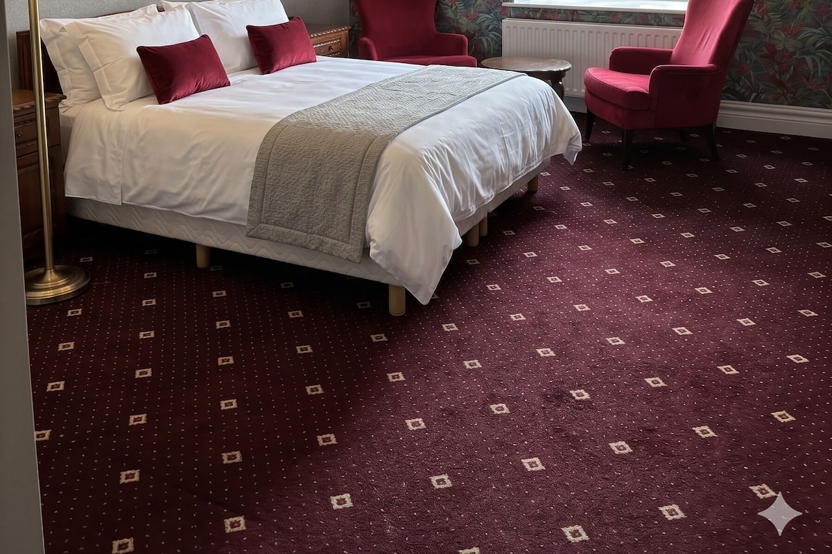 A hotel room with a large bed, two red chairs, a window with a view, and a ceiling light fixture.