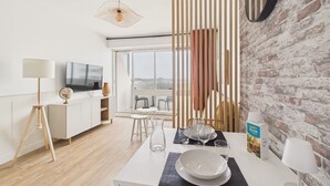 A modern living room with a dining area, a television, and a view of the city. - Sea view for 4 by the beach (Saint-Hilaire-de-Riez)