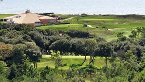 A golf course with a clubhouse, surrounded by dense trees and a body of water in the background. - Sea view for 4 by the beach (Saint-Hilaire-de-Riez)