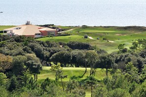 A golf course with a clubhouse, surrounded by dense trees and a body of water in the background. - Sea view for 4 by the beach (Saint-Hilaire-de-Riez)