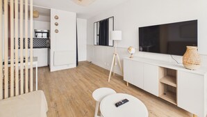 A modern living room with a flat-screen TV, a dining area with a table and chairs, a kitchen with a microwave, and a ceiling fan. - Sea view for 4 by the beach (Saint-Hilaire-de-Riez)
