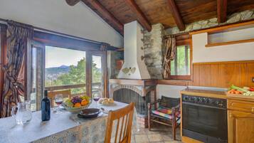 Una cocina rústica con chimenea de piedra, armarios de madera y un comedor con una mesa preparada para dos.