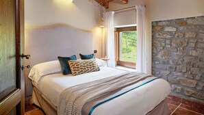 A bedroom with a stone wall, a bed with white bedding, a wooden ceiling, and a window with curtains. - Tenuta Valdea (Firenzuola)
