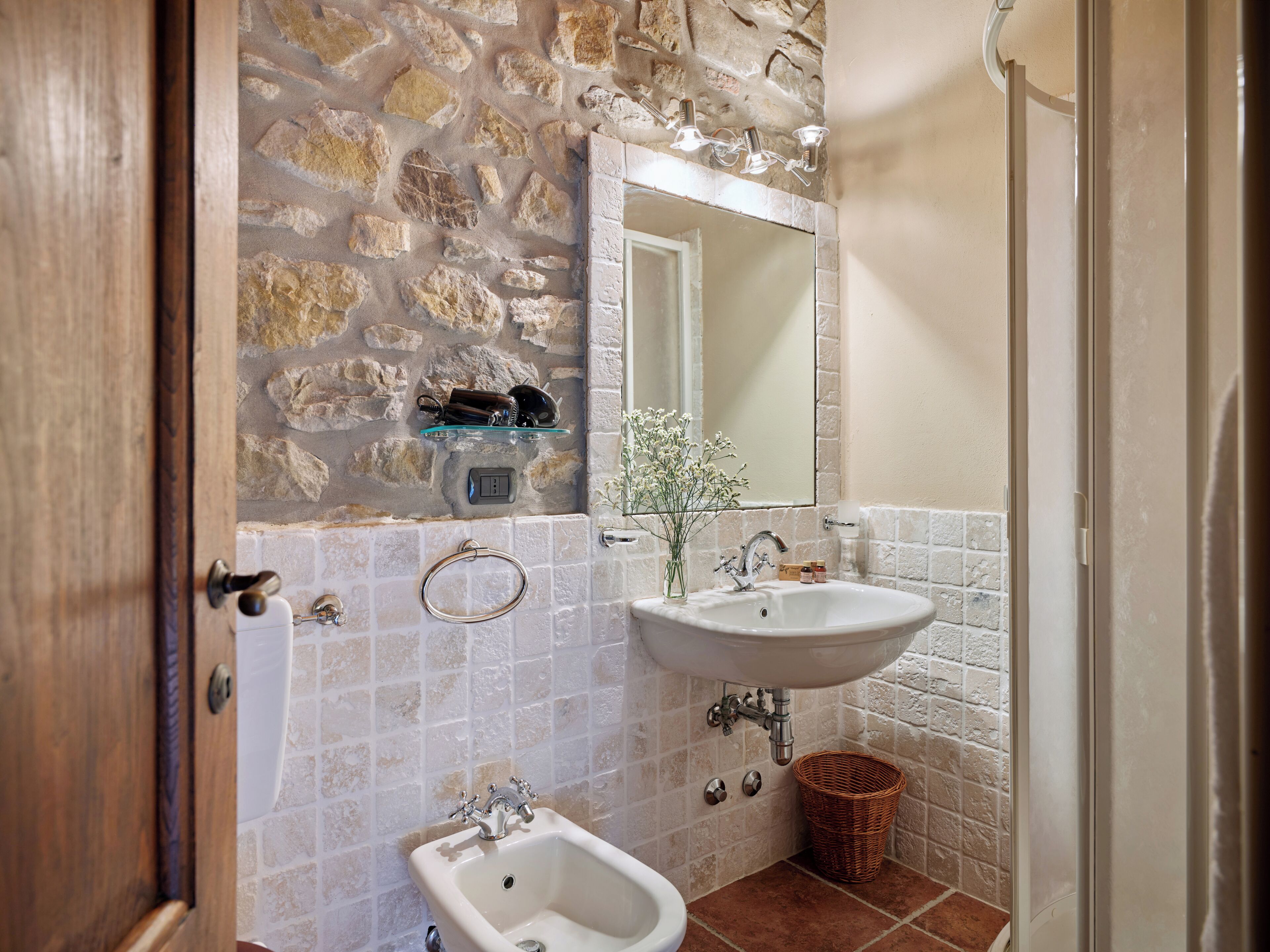 Un baño con pared de piedra, un lavabo blanco, un bidé y un espejo.