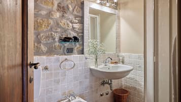 Un baño con pared de piedra, un lavabo blanco, un bidé y un espejo.