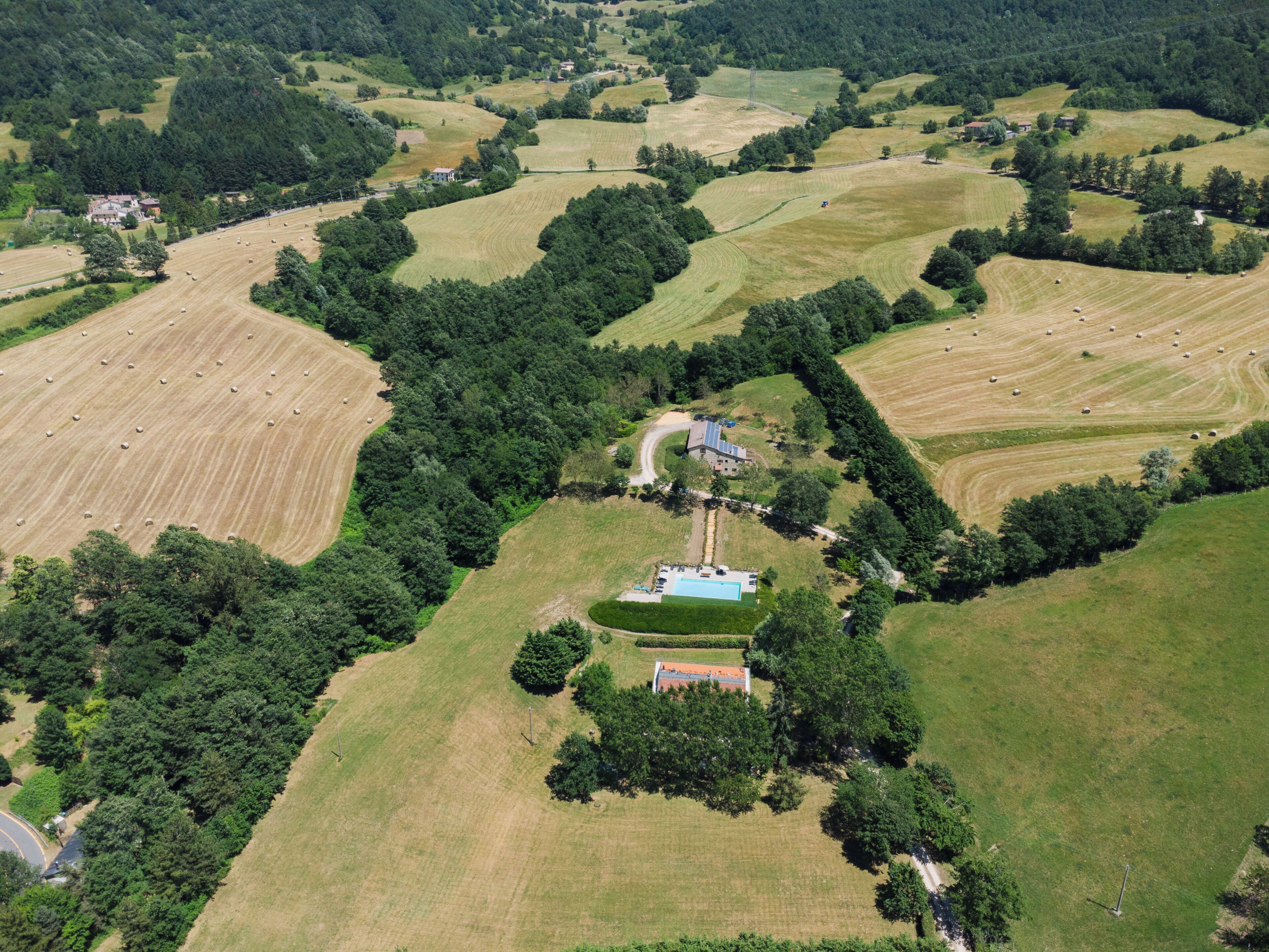 An aerial view of a rural landscape with fields, trees, and a small building with a swimming pool.