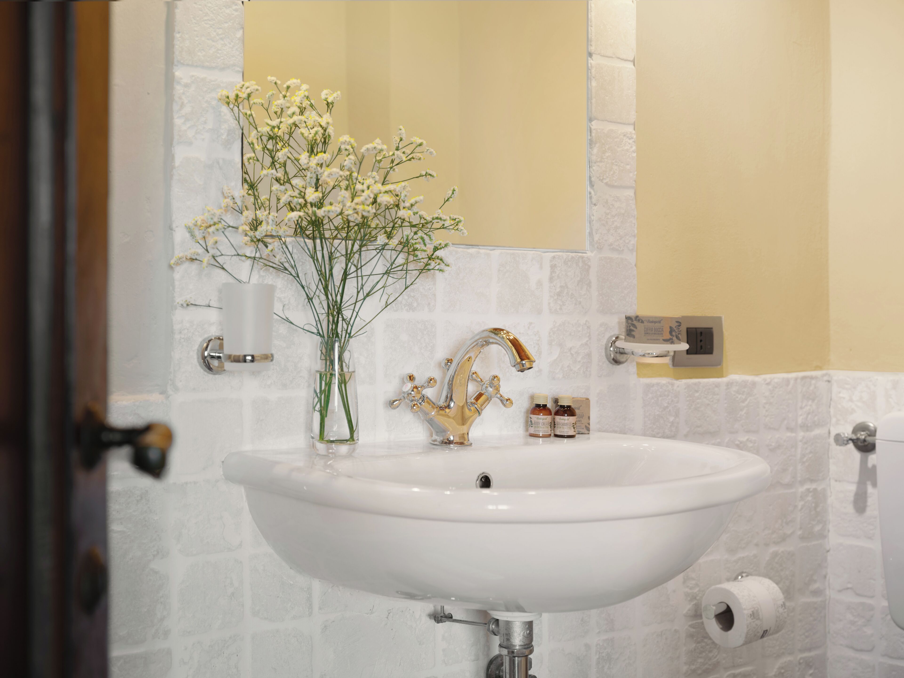 Ein Badezimmer mit Waschbecken, goldenem Wasserhahn und einer Vase mit weißen Blumen.