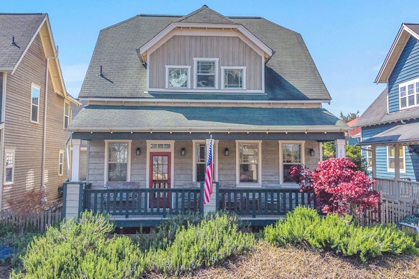 Charming coastal cottage with wraparound porch and manicured gardens in a picturesque neighborhood setting.