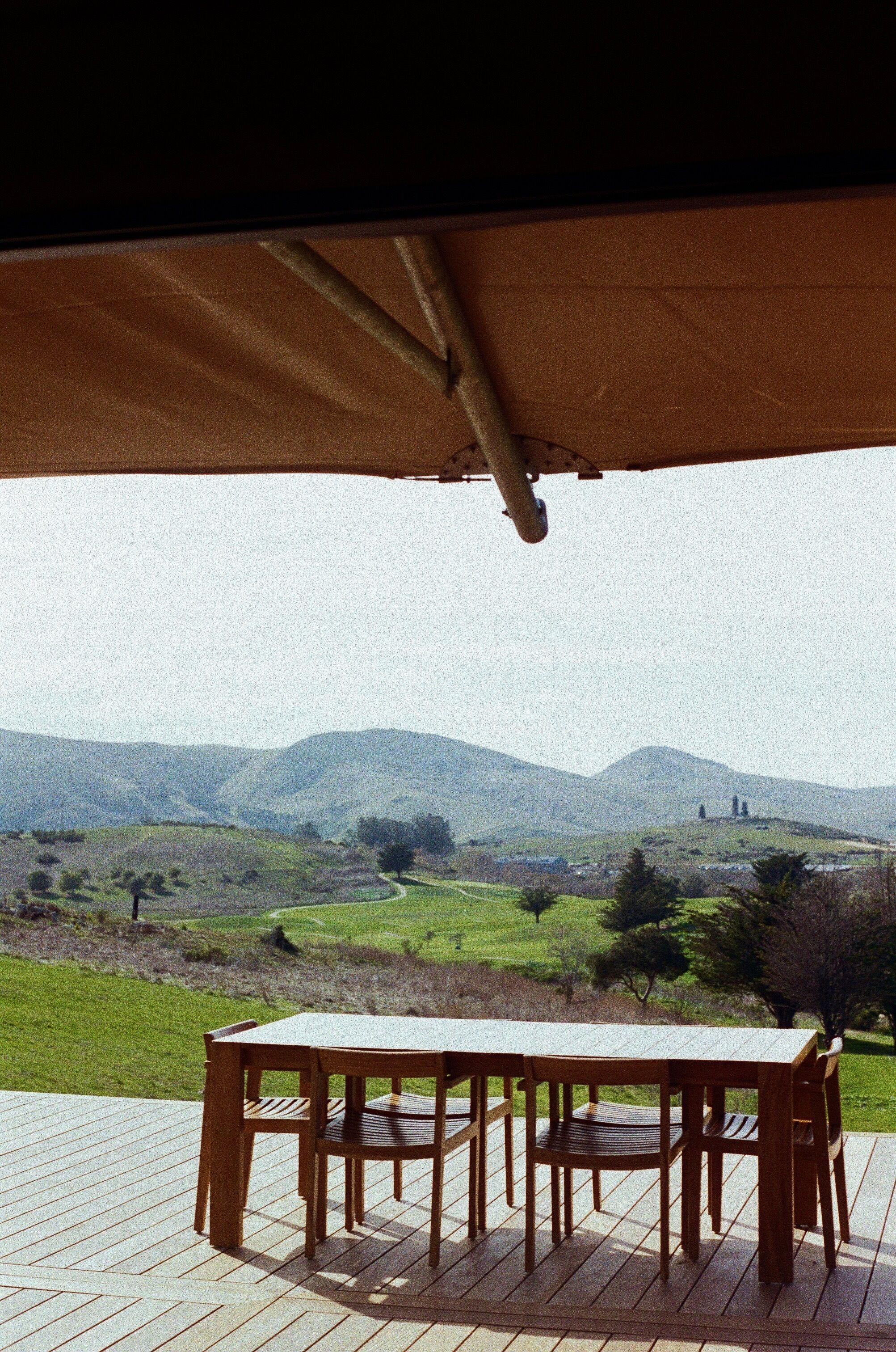 Eine Holzterrasse mit Tisch und Stühlen mit Blick auf eine hügelige Landschaft.