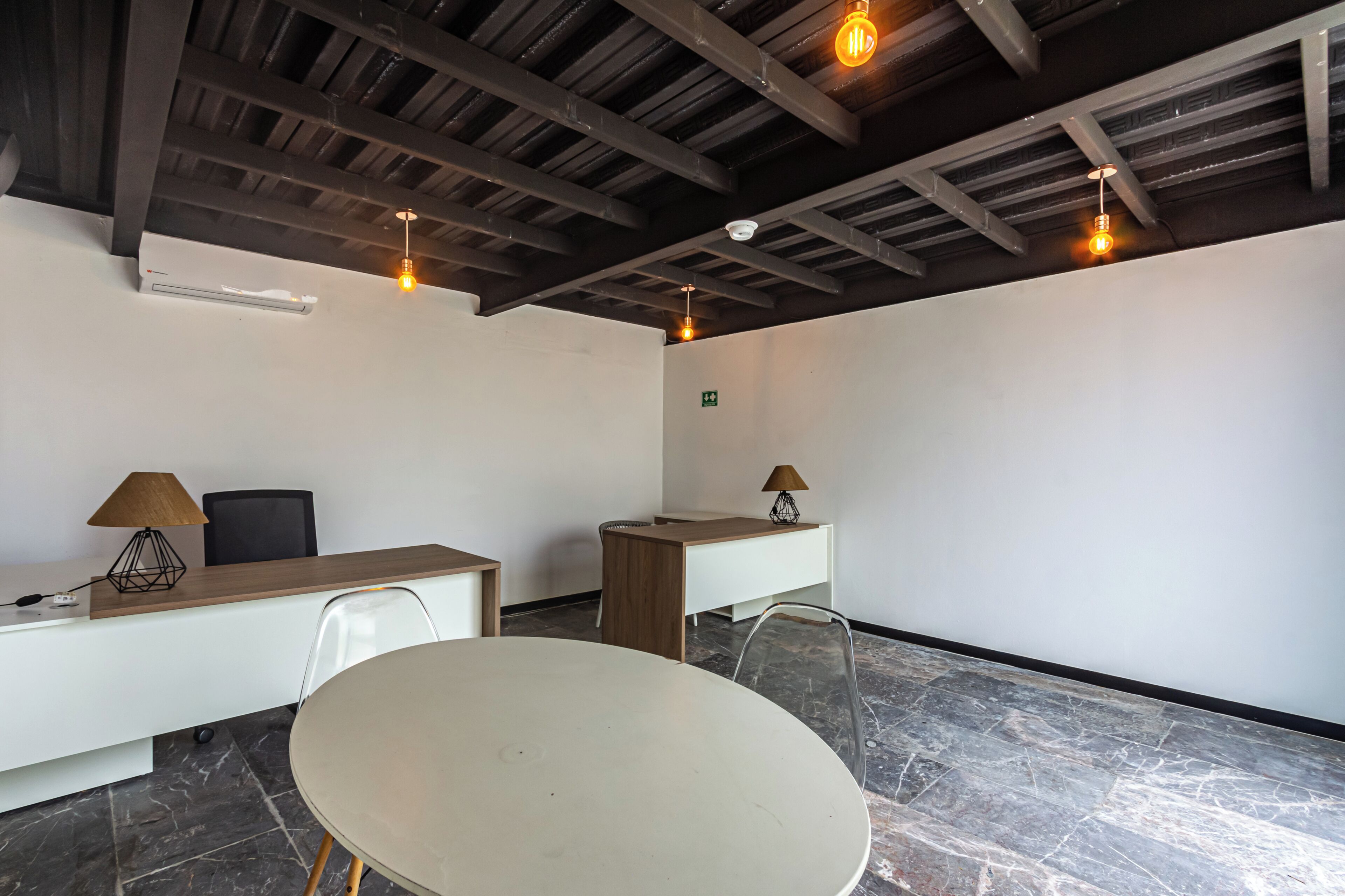 Een vergaderruimte met een ronde tafel, twee bureaus, stoelen en hanglampen.