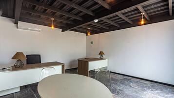 Een vergaderruimte met een ronde tafel, twee bureaus, stoelen en hanglampen.