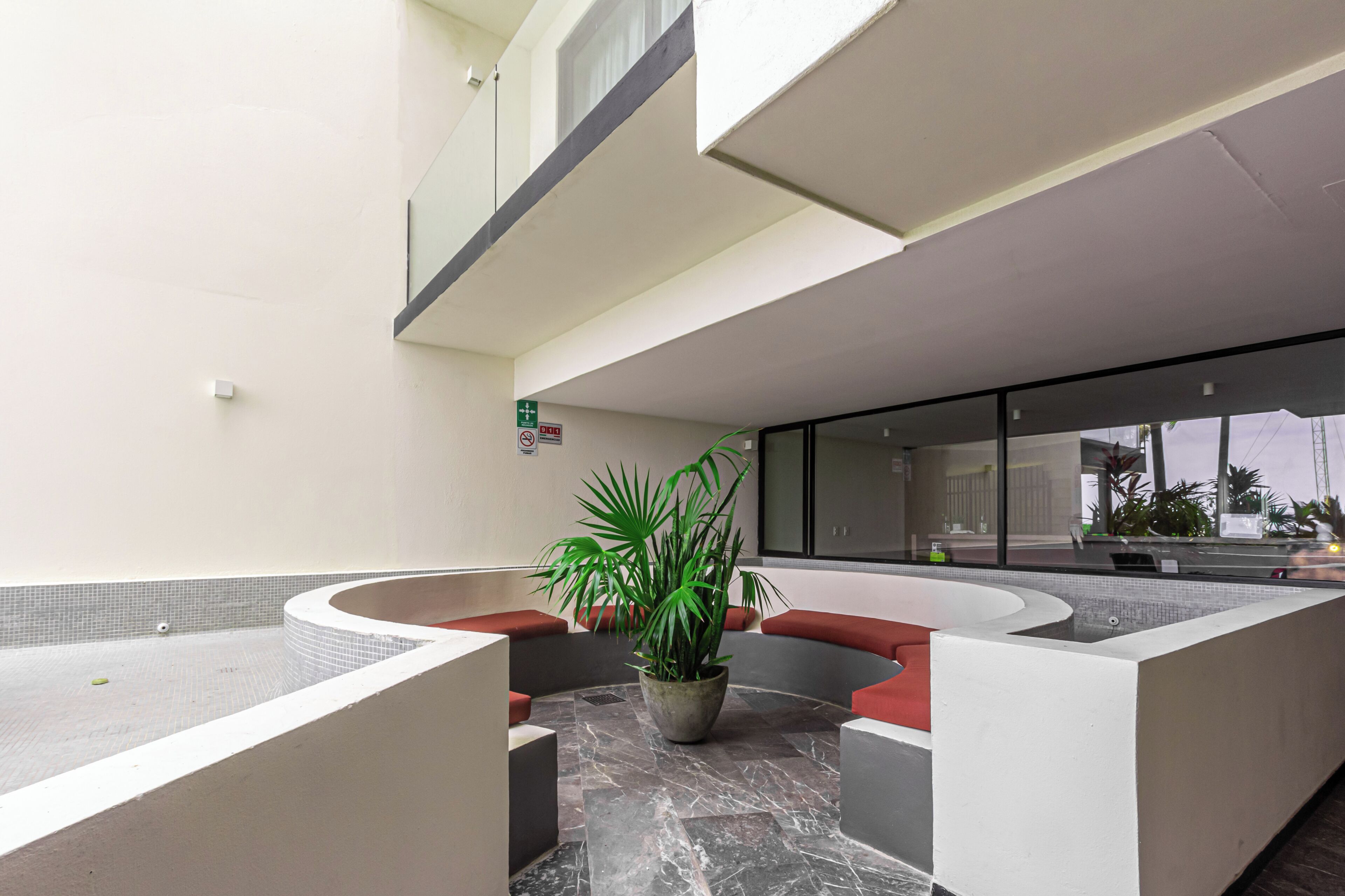 Een moderne lobby met een gebogen zithoek, een potplant en een glazen scheidingswand.
