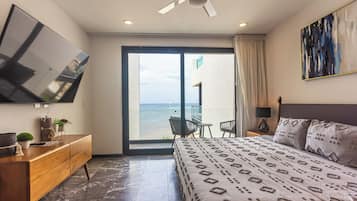 Quarto de hotel moderno com cama, televisão, varanda e vista para o mar, e ventoinha no teto.