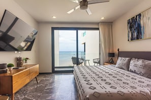 Ein modernes Hotelzimmer mit Bett, Fernseher, einem Balkon mit Meerblick und einem Deckenventilator.