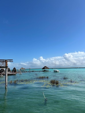 A clear blue sky, calm turquoise waters, and overwater bungalows with thatched roofs.