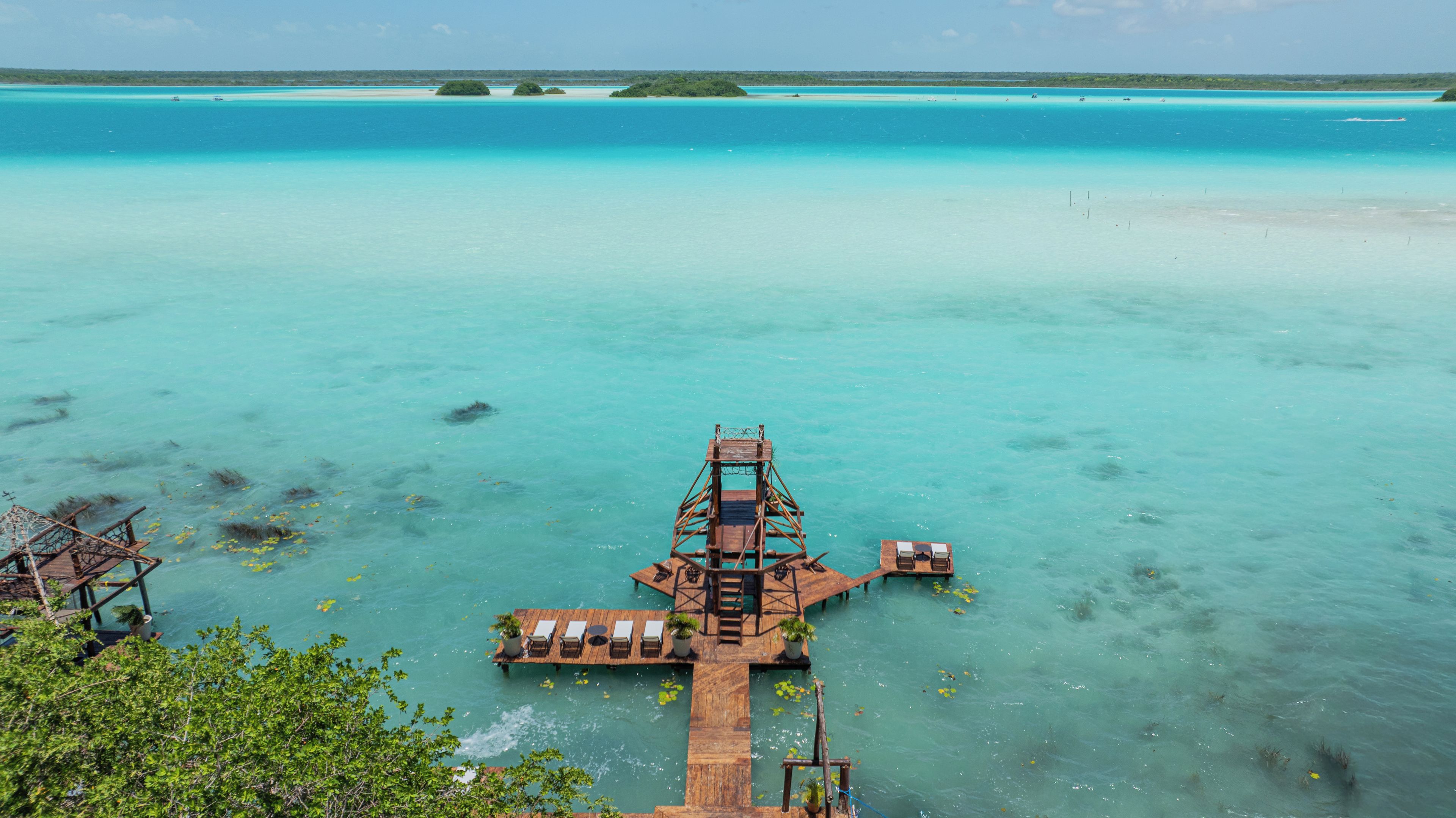 Een houten pier die zich uitstrekt in turquoise water, met een klein steiger en ligbedden.
