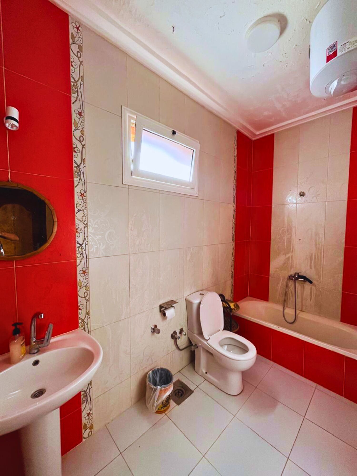 A bathroom with a toilet, sink, shower, and a small window.