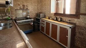 Une cuisine équipée d’une cuisinière à gaz, d’un four à micro-ondes et d’une fenêtre avec des stores.