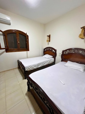 Quarto com duas camas de madeira, um guarda-roupa e um aparelho de ar condicionado.