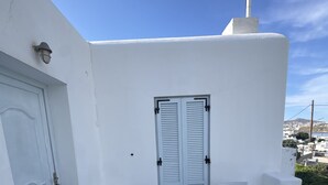 A white outdoor patio with a table and chairs, a door, and a view of the town. - Casa Bianca Mykonos (Ornos)