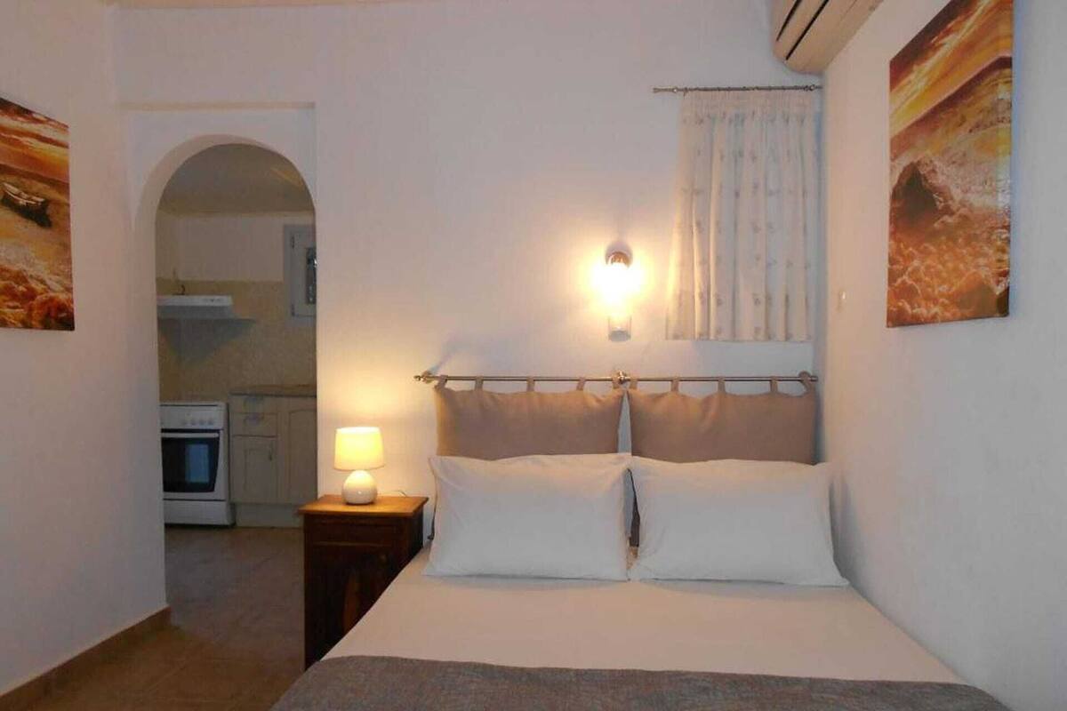 A bedroom with a bed, bedside lamp, and a view of a kitchen.