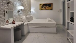 A bedroom with a stone wall, a bed, a bedside table, a lamp, and a painting. - Casa Bianca Mykonos (Ornos)