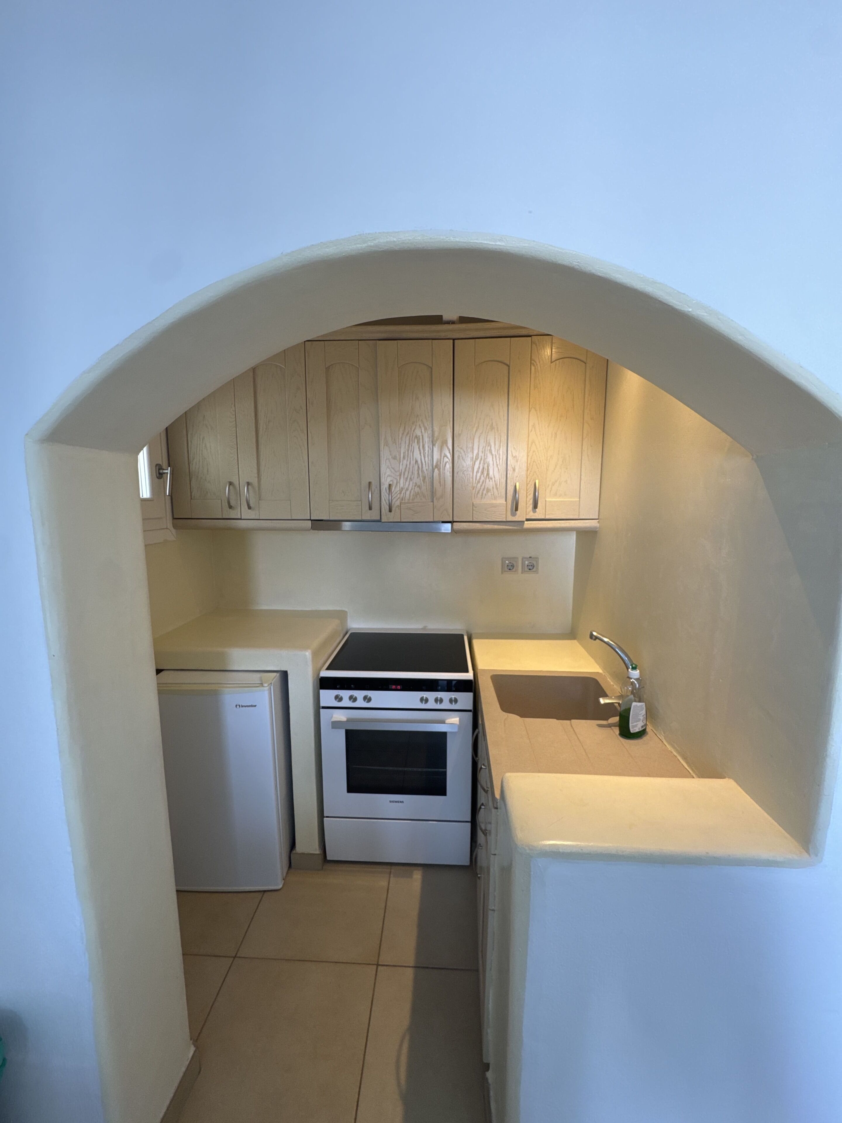 A compact kitchen with a built-in oven, a small refrigerator, and wooden cabinets under a sloped ceiling.