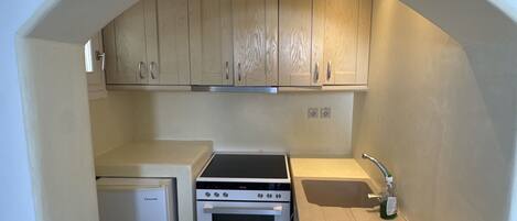 A compact kitchen with a built-in oven, a small refrigerator, and wooden cabinets under a sloped ceiling.