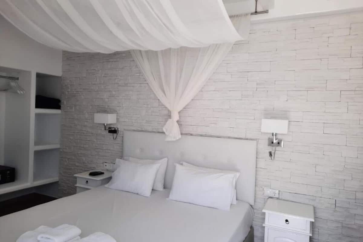 Un dormitorio moderno con una cama blanca, cortinas blancas, una pared con diseño de ladrillo y una mesita de noche blanca con una lámpara.