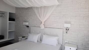 Une chambre à coucher moderne avec un lit blanc, des rideaux blancs, un mur décoré d’un motif en briques et une table de chevet blanche avec une lampe.