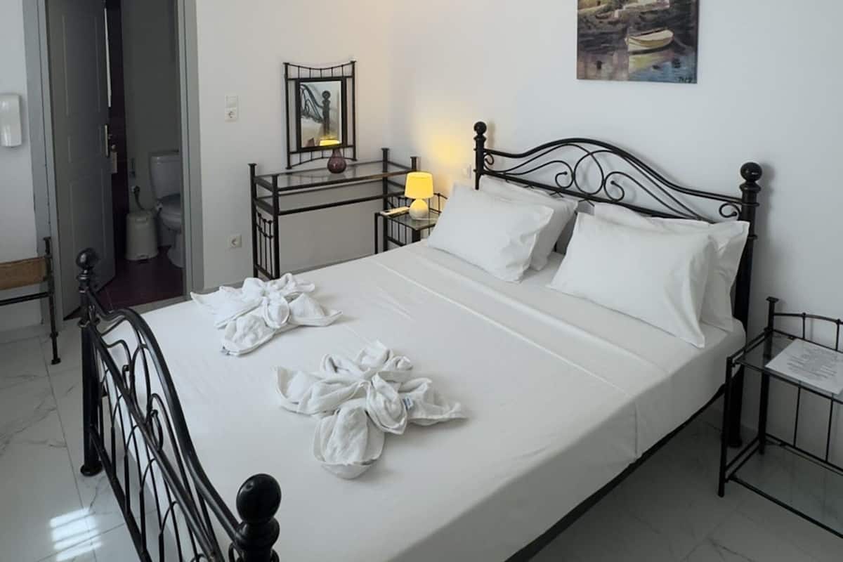 A hotel room with a bed, a painting, a lamp, and a door leading to a bathroom.