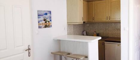 A kitchen with wooden cabinets, a white countertop, and a small bar area with stools.