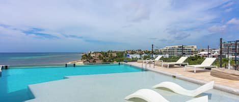 A swimming pool with clear blue water, white lounge chairs, and a view of the ocean.
