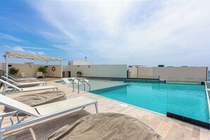Ein Pool auf dem Dach mit Liegestühlen, einem Rettungsring und blauem Himmel.