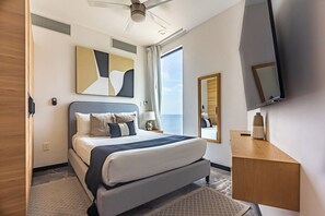 Ein modernes Hotelzimmer mit Bett, Schreibtisch, Flachbildfernseher, Deckenventilator und großem Fenster.