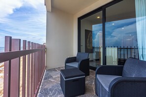 Ein Balkon mit Blick auf das Meer, eine Glastür und zwei Korbstühle.