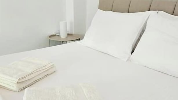 Un letto rifatto con lenzuola bianche, un comodino con una lampada e una testiera.