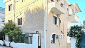 Un edificio di due piani con tetto piatto, ingresso carrabile e un piccolo giardino con piante in vaso.