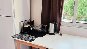 Una piccola cucina con frigorifero, un tavolo con sottotavolo, un bollitore e una finestra con tende.