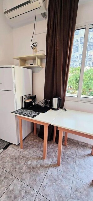 A small kitchen with a refrigerator, a table with a placemat, a kettle, and a window with curtains. - PH Azure Horizon Residences G/1 (Sarandë)